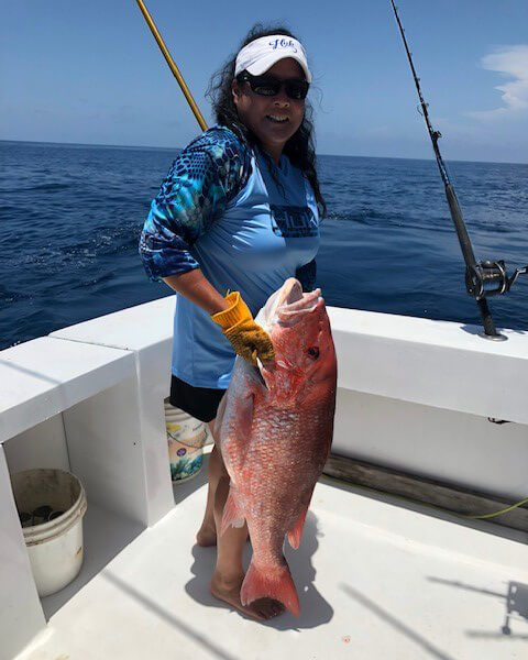 Matilda Jeung holds a large red fish by the gills on her fishing boat