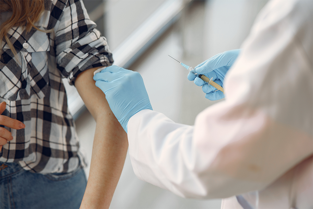 Doctor wearing gloves gives vaccination to person in plaid shirt